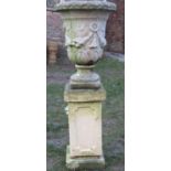 A weathered cast composition stone garden urn with repeating floral swag detail, raised on an