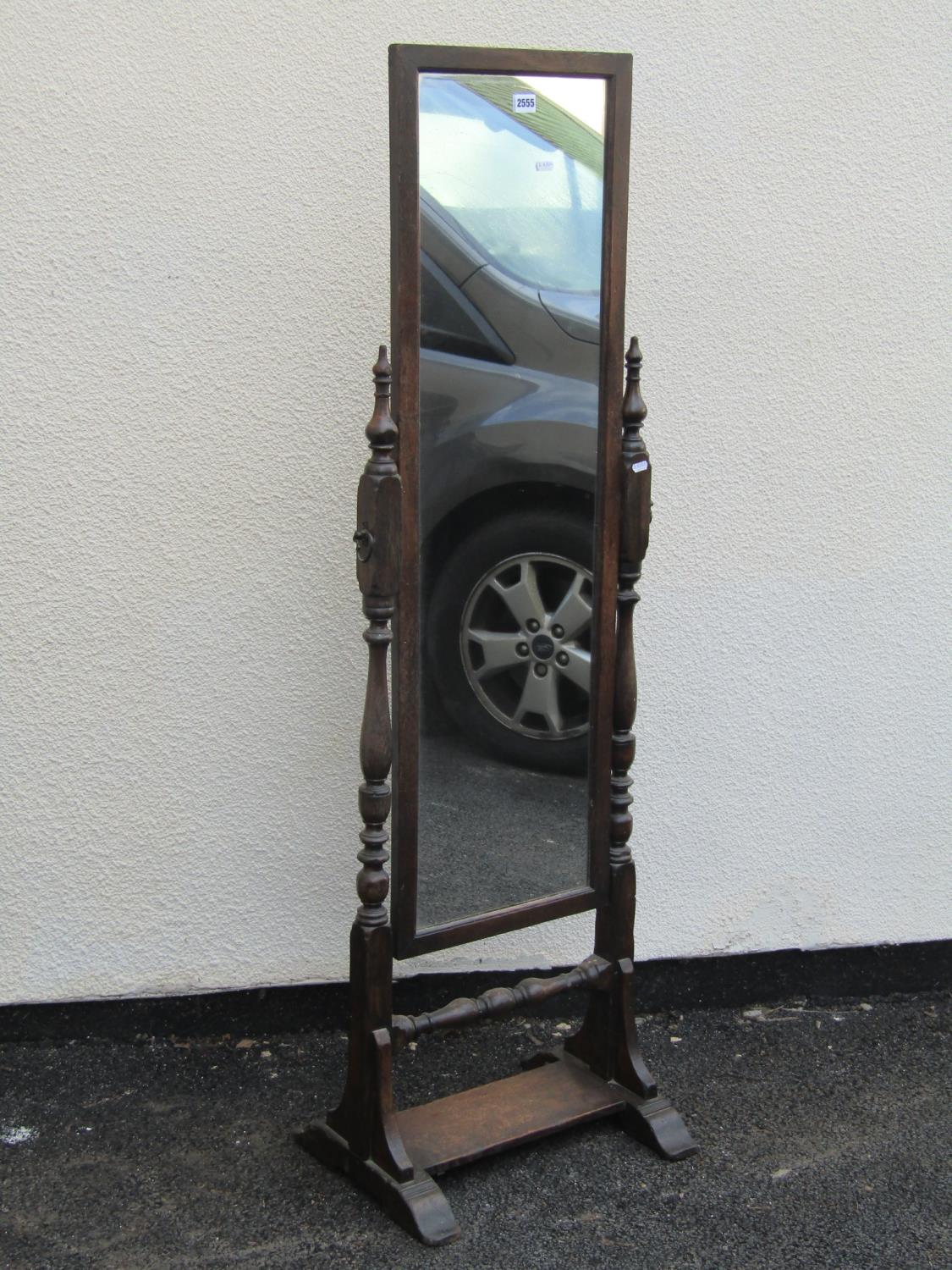 An old English style oak cheval glass raised on turned column supports and platform base, together