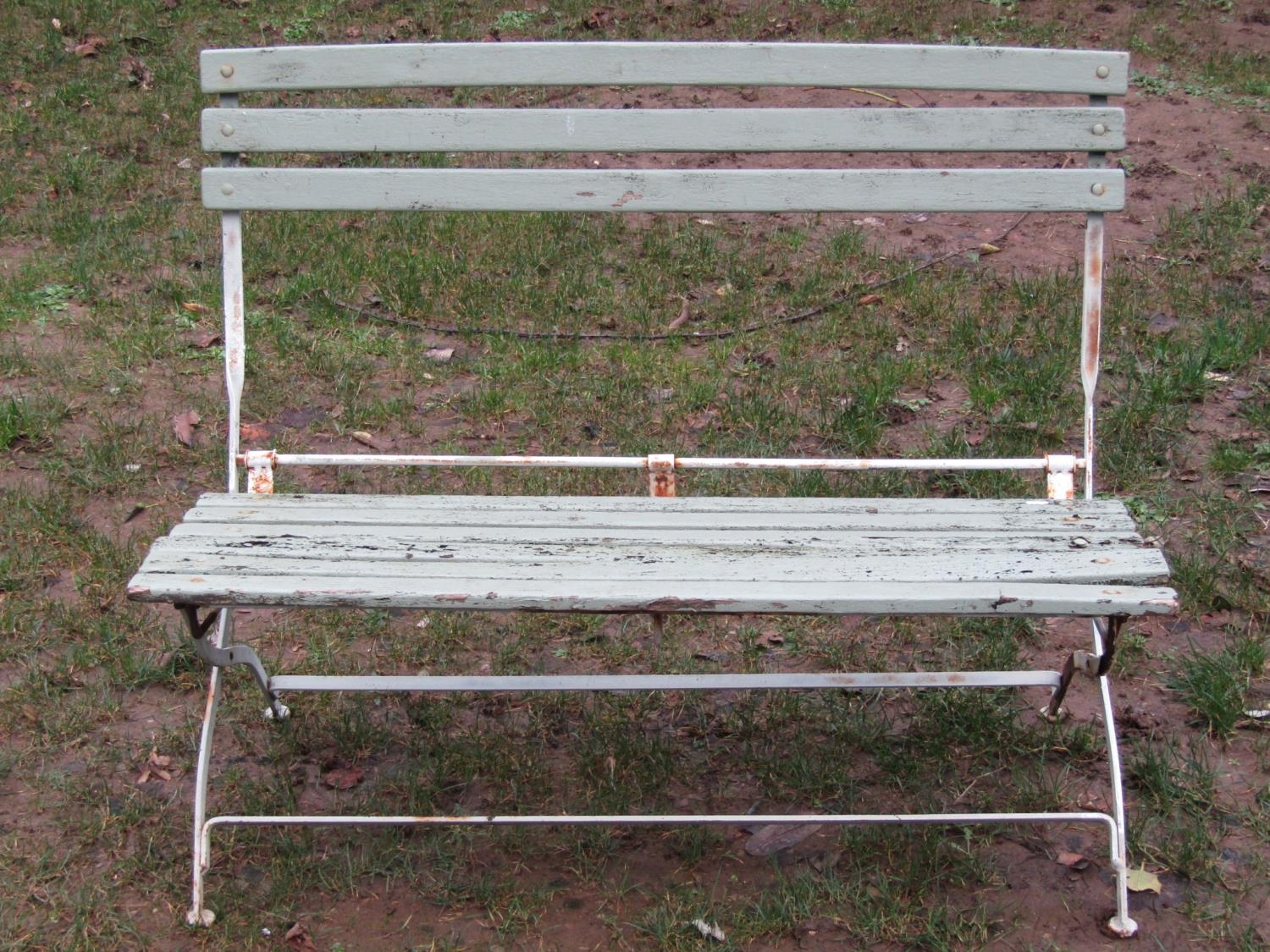 A painted and weathered iron framed folding two seat garden bench with painted wooden slats, (af),