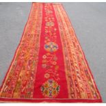 A Turkey Runner with a central floral and lozenge panel on a red ground,460cm x 140cm approx.