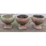 A set of three weathered simulated terracotta garden urns with circular fluted bowls and square