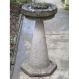 A weathered cast composition stone bird bath of circular form raised on a conical shaped pedestal