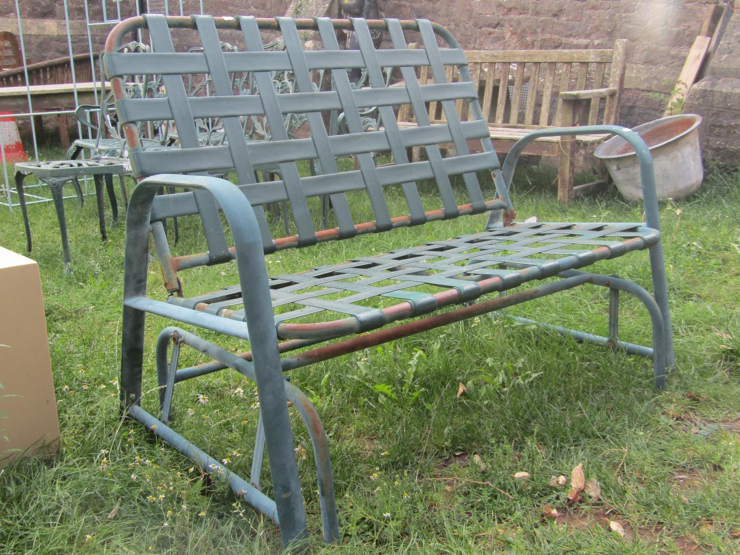 A green painted tubular steel framed two seat rocking garden bench with interlaced strapwork seat