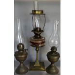 An art deco brass oil lamp base supporting a clear glass font with twin burner and two further brass