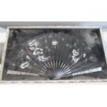 A framed black ladies fan decorated with flowers set within a glass frame