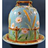 A George Jones majolica cheese dome with blue sky background against corn ears, daisies,