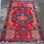 A slightly worn Kazak carpet with three stepped interlocking lozenges, on a red ground. 188cm x