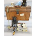 A vintage tin car trunk containing a coffee grinder, a table top meat mincer, a vintage mahogany