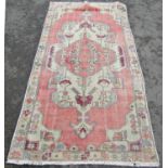 A Persian carpet with a stylised floral central medallion in hues of pink and cream. 220cm x 115cm