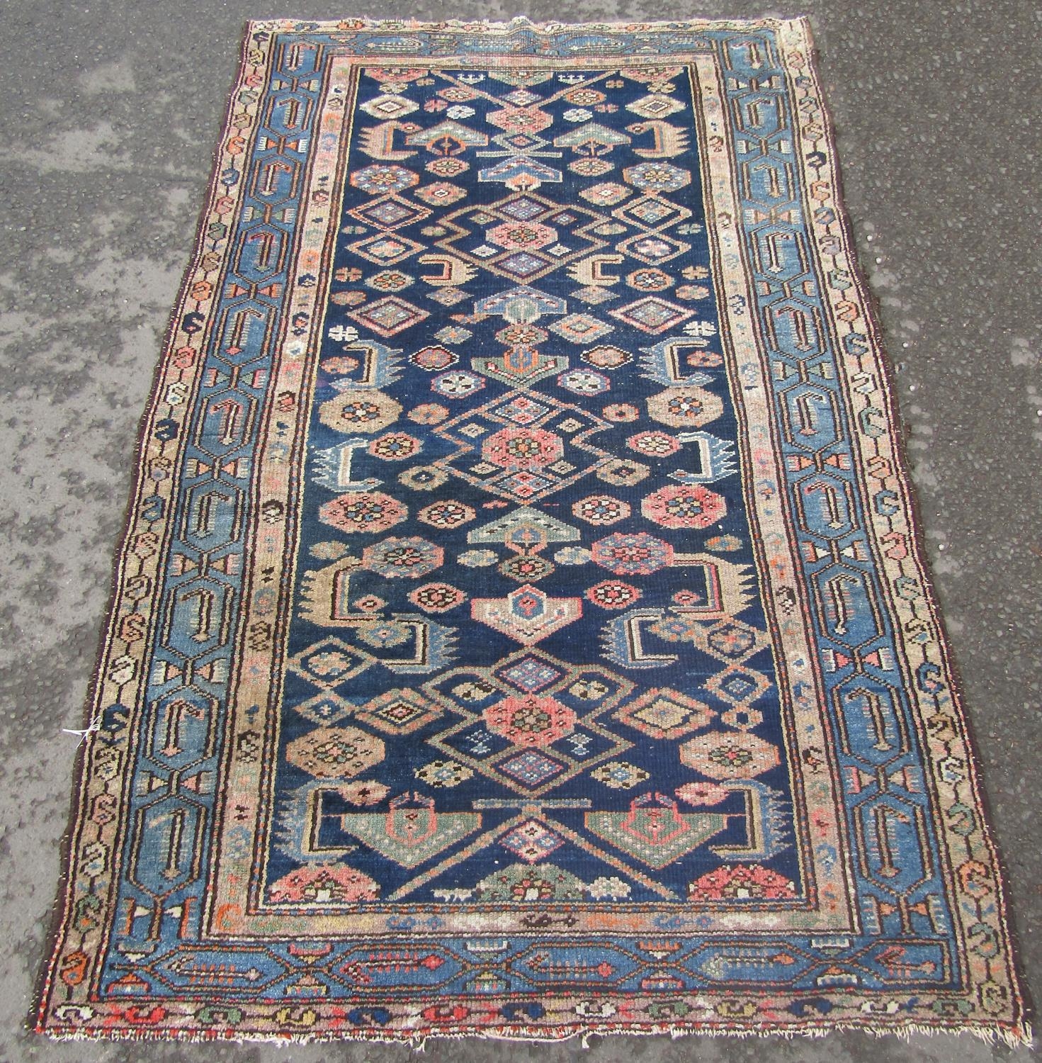 An old Malayer carpet with a repeating geometric pattern on a blue ground