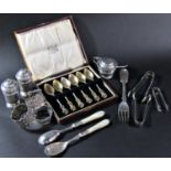 A mixed selection of silver tableware including a three piece condiment set, three sugar tongs,