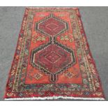 A Kazak design carpet with two interlocking stepped medallions on a madder field, 211cm x 128cm