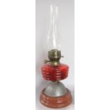 An oil lamp with a red ribbed glass font, lacks a shade.