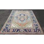 A Heriz carpet with a broad blue flower shaped central medallion on a pale cream ground, signed in a