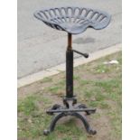 A cast iron adjustable high stool with tractor type seat over a foot rest with swept and scrolled