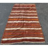 A North African flat weave carpet in horizontal stripes of ochre, pink and brown interspersed with