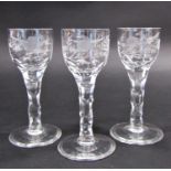 Three 19th century floral and bird engraved, cut glass wine glasses on faceted stems 14.5cm tall.