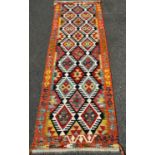 A Chobi Kilim Runner with a central panel of diamond medallions defined in black borders, 252cm x