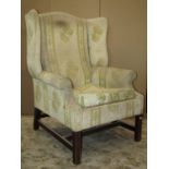 A Georgian style wing armchair raised on square cut and moulded supports united by stretchers, (