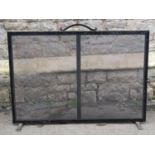 An iron framed fire guard of rectangular form with wire mesh panel and open simple scroll looped