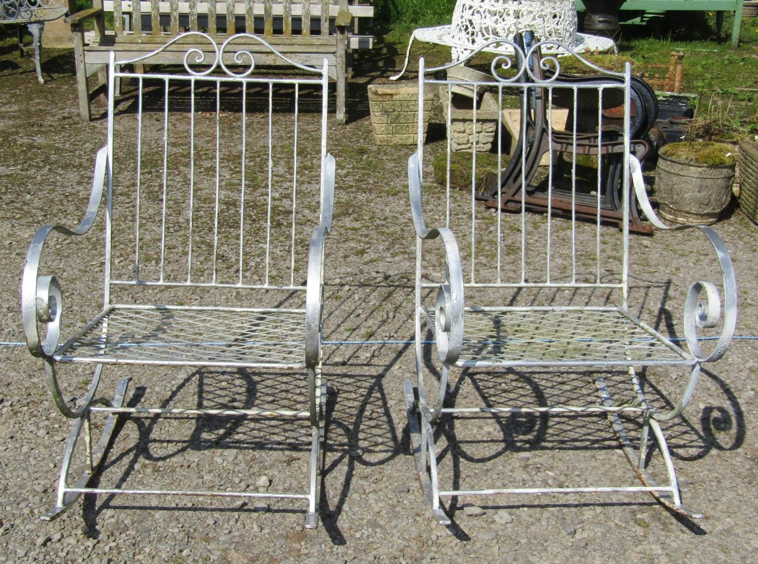 A pair of decorative painted ironwork garden rocking chairs with open scrolled arms and lattice