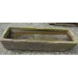 A weathered rectangular carved natural stone trough with rounded front corners and dished