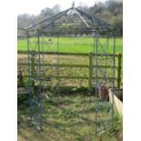 A vintage ironwork gazebo, with four main uprights, supporting an octagonal pointed canopy with