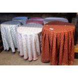 Six various circular occasional tables with material throw covers, together with a wicker basket and