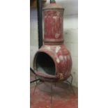 A large two sectional clay chimenea with fluted detail, complete with cap, raised on an ironwork