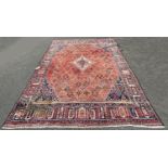 A Middle Eastern design carpet with a repeating geometric design on a pale red ground, worn in