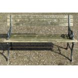 A two seat garden bench with weathered wooden lathes raised on decorative pierced cast iron end