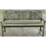 A weathered hardwood three seat garden bench with slatted seat beneath a decorative lattice panelled