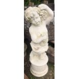 A cast composition stone garden ornament in the form of a standing cherub holding bunches of
