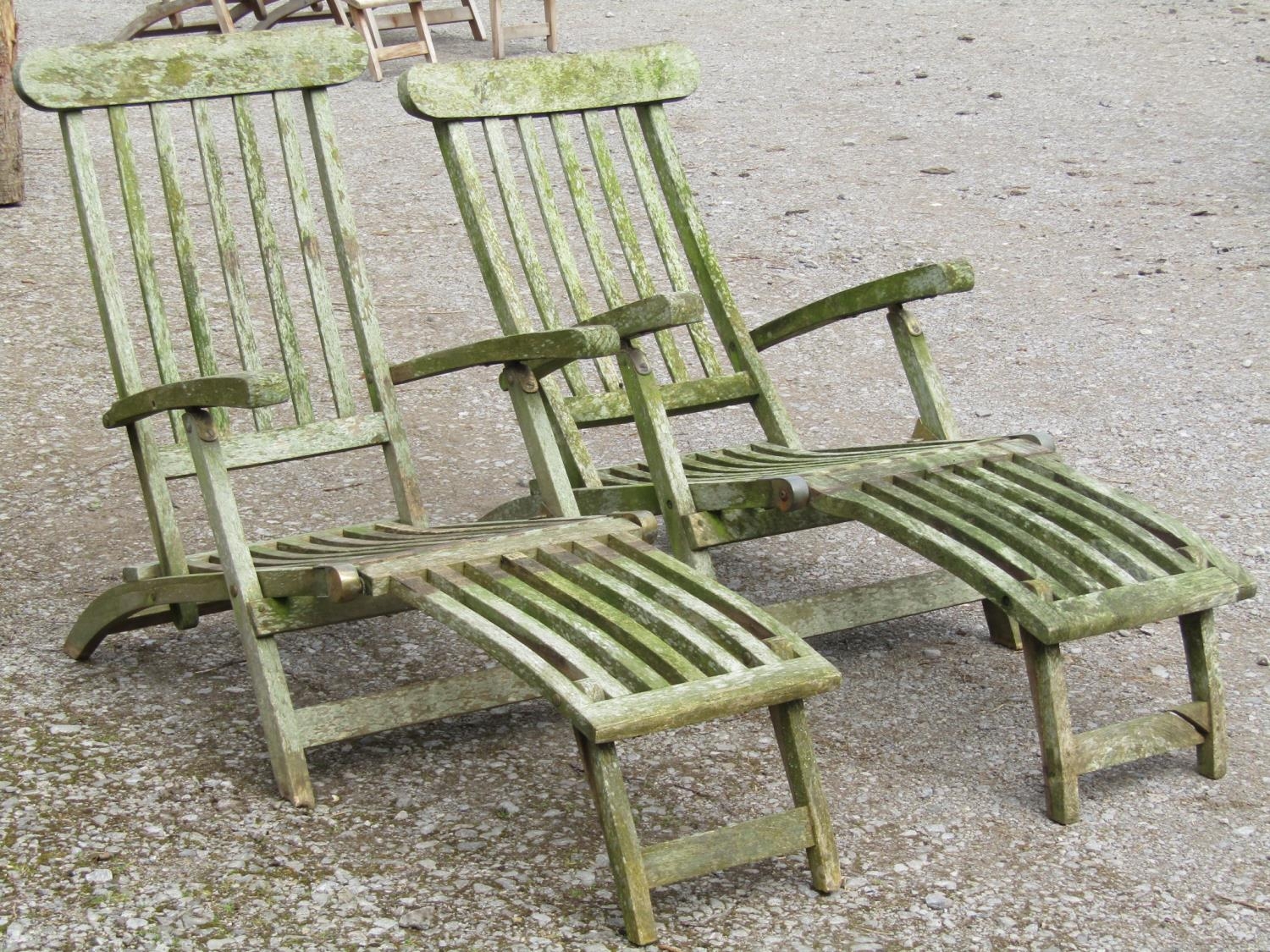 A pair of well weathered teak folding garden steamer type lounge chairs with slatted seats, backs