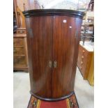 A Georgian mahogany bow fronted hanging corner cupboard enclosed by a pair of rectangular doors with