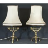 A pair brass lyre shaped table lamps raised on three legs.