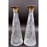 A pair of silver collared cut glass conical shaped decanters, lacking stoppers.