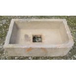 A weathered rectangular natural stone trough with single rounded corner and central square drain
