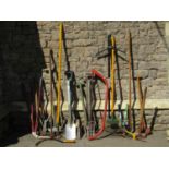 A collection of long handled gardening tools, spades, forks, rakes, bow saw etc