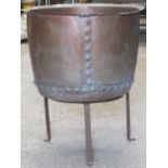 An old copper with flared rim and pop rivetted seams, raised on a simple iron work stand, 53cm