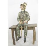 A cold painted figure of a monocled dapper man with top hat and cane seated on a table, 13cm tall.