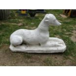 A painted cast composition stone garden/pier ornament in the form of a recumbent greyhound/whippet