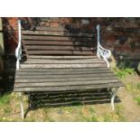 A two seat garden bench with weathered timber lathes raised on a pair of decorative painted cast