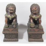 A pair of Chinese bronze and lacquered lion dogs with raised paws, set on plinths, 15 cm wide x 20