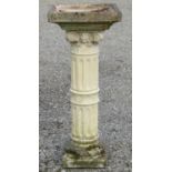 A weathered cast composition stone two sectional bird bath, the square top raised on a fluted