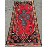 A narrow Kazak runner with a central blue extended diamond medallion and stylised flowers on a red