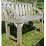 A weathered hardwood two seat garden bench with slatted seat, back and curved arms (stamped to