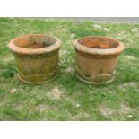 A pair of weathered squat cylindrical terracotta planters with repeating tree and rolling