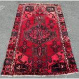 A Middle Eastern carpet with an extended central medallion on a predominantly red ground 183 cm x