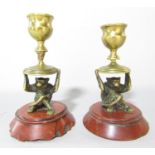 A pair of continental brass monkeys holding aloft candlesticks sat on red marble bases 12cm high. (